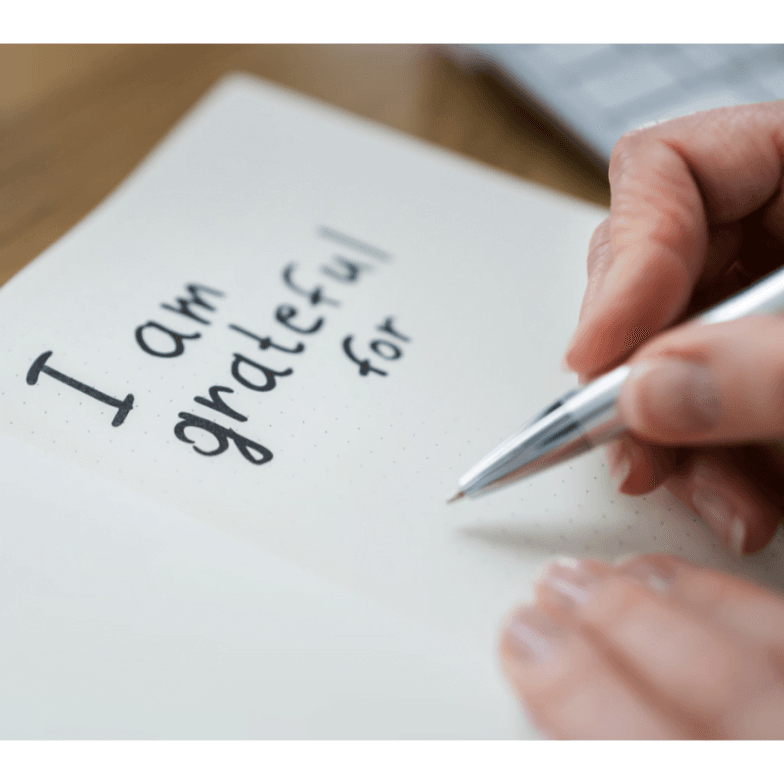 Image of a person's hand about to finish their sentence in a journal. The words "I am grateful for" are already written on the page.