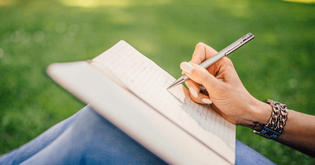 Person sitting outside writing in a journal.