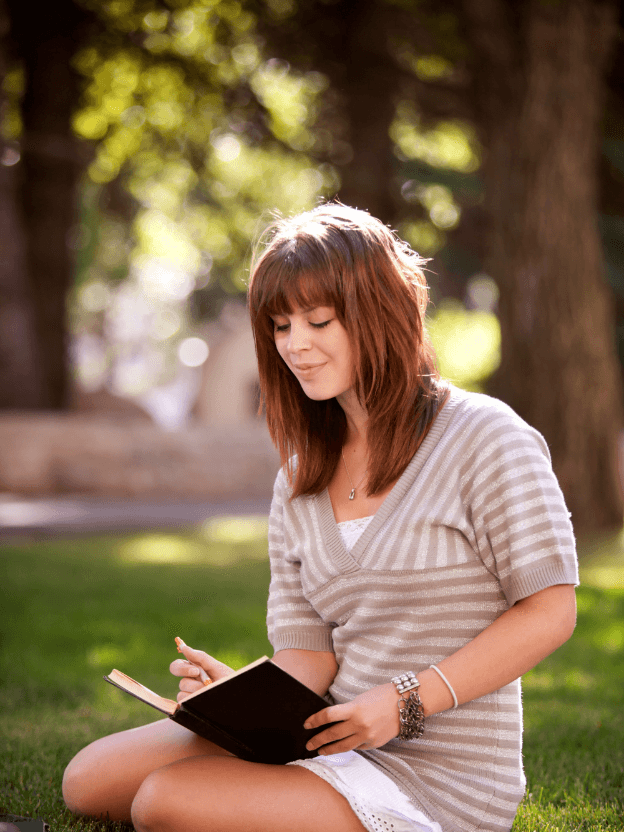 Woman sit outside on a sunny day writing in a journal.