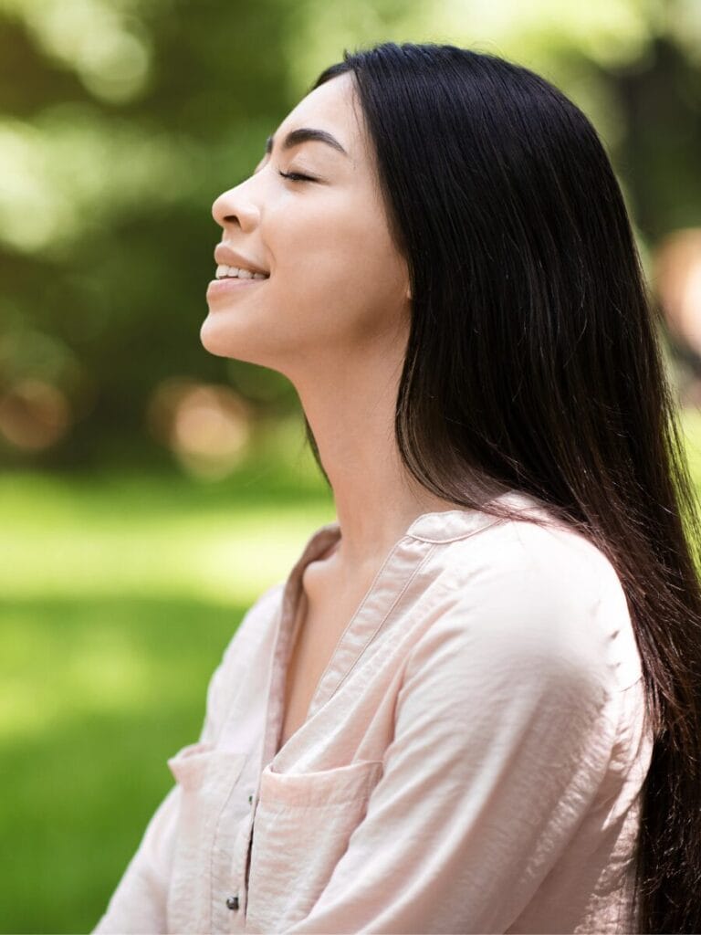 Image of a woman sitting outdoors with her eyes closed, smiling.