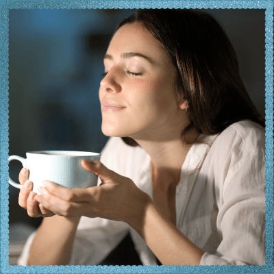 **Alt Text:**Woman with eyes closed holding a cup, appearing peaceful and relaxed while enjoying the aroma.